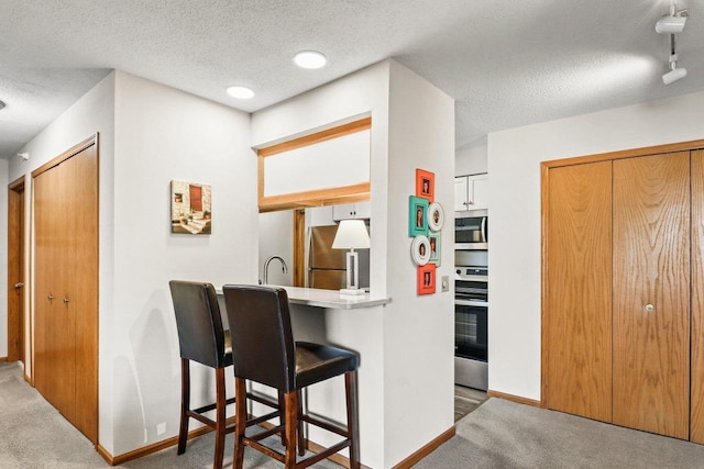 kitchen with carpet, baseboards, appliances with stainless steel finishes, and a textured ceiling