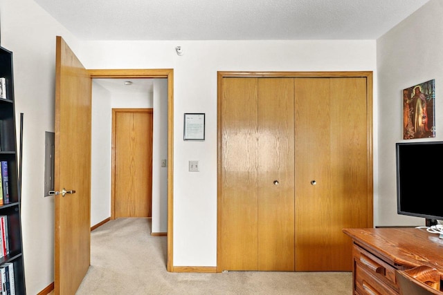 bedroom with a textured ceiling, light colored carpet, a closet, and baseboards