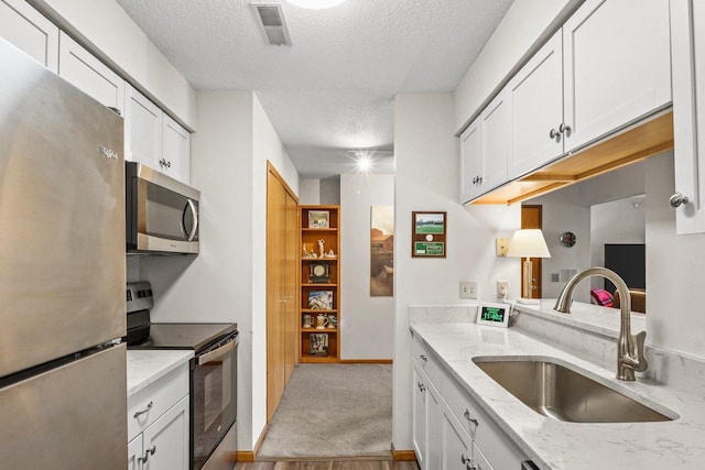 kitchen with visible vents, light colored carpet, appliances with stainless steel finishes, white cabinetry, and a sink