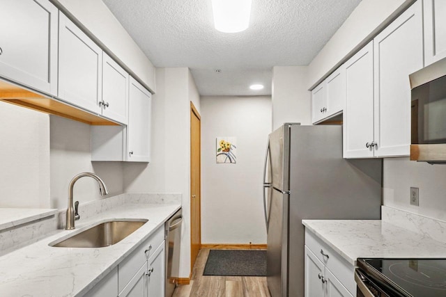 kitchen with light stone countertops, a sink, light wood-style floors, appliances with stainless steel finishes, and white cabinetry