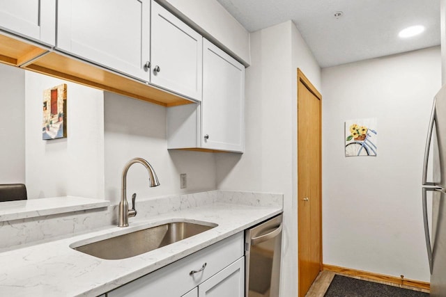 kitchen with a sink, light stone counters, appliances with stainless steel finishes, white cabinets, and baseboards