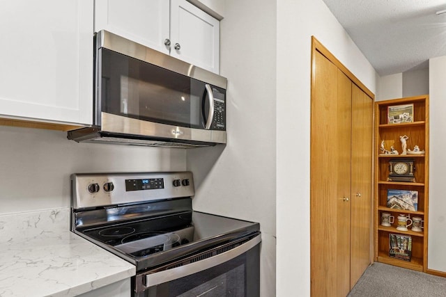 kitchen with light stone counters, carpet, appliances with stainless steel finishes, and white cabinets