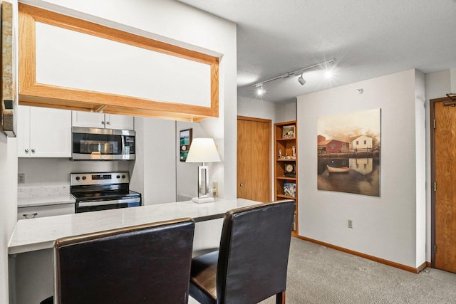 kitchen with baseboards, light carpet, light stone counters, stainless steel appliances, and white cabinetry