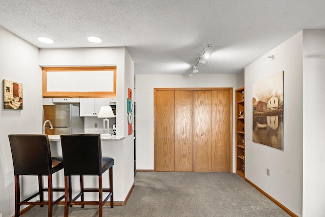 kitchen with a breakfast bar area, baseboards, carpet floors, freestanding refrigerator, and a textured ceiling