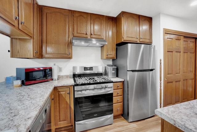 kitchen featuring brown cabinetry, stainless steel appliances, light countertops, light wood-style floors, and under cabinet range hood