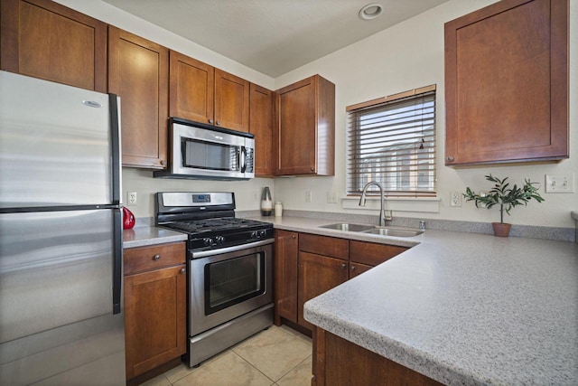 kitchen featuring light tile patterned flooring, a sink, light countertops, appliances with stainless steel finishes, and brown cabinets