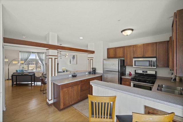 kitchen featuring brown cabinetry, a peninsula, a sink, appliances with stainless steel finishes, and light wood-type flooring