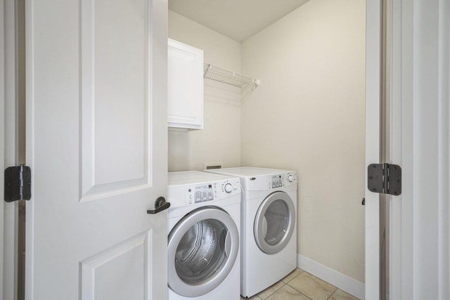 washroom featuring light tile patterned floors, baseboards, washing machine and dryer, and cabinet space