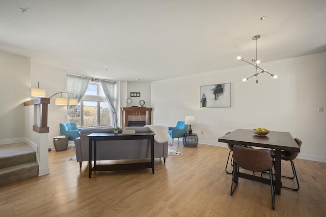 living area with stairway, baseboards, an inviting chandelier, a tile fireplace, and light wood-style floors