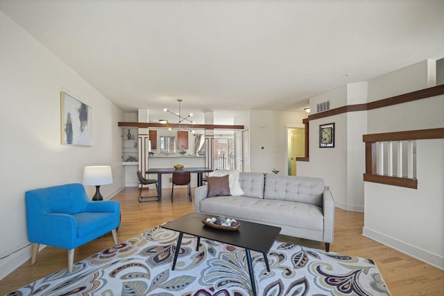 living room featuring visible vents, baseboards, light wood-style floors, and a chandelier