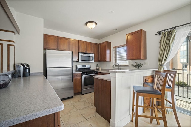 kitchen with a kitchen bar, brown cabinets, appliances with stainless steel finishes, a peninsula, and light countertops