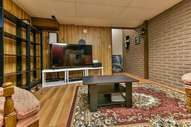 living area featuring brick wall, wood finished floors, wood walls, and a drop ceiling