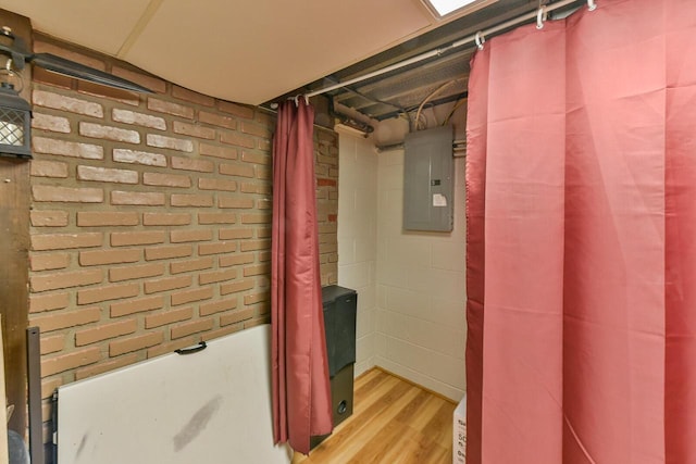 full bathroom featuring a shower with curtain, electric panel, wood finished floors, brick wall, and a bathtub