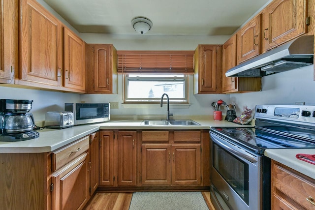 kitchen with under cabinet range hood, appliances with stainless steel finishes, light countertops, and a sink