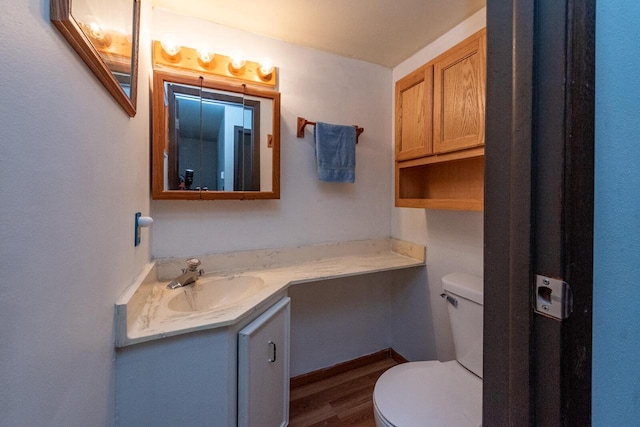 half bath with toilet, wood finished floors, and vanity