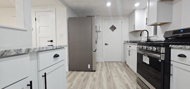 kitchen featuring white cabinetry, light wood-style flooring, light stone countertops, and stainless steel appliances