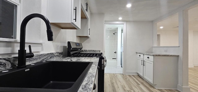 kitchen featuring a sink, light stone counters, light wood-style floors, white cabinets, and gas range