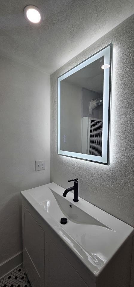 bathroom with a textured ceiling, vanity, and a textured wall