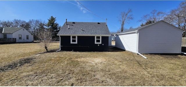 back of house featuring an outdoor structure, a lawn, and a shingled roof