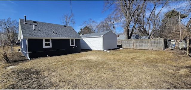 back of house featuring a storage unit, an outbuilding, fence, a yard, and a shingled roof