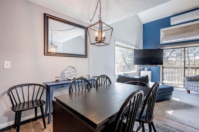 dining area featuring a wall mounted air conditioner, a textured ceiling, wood finished floors, an inviting chandelier, and baseboards