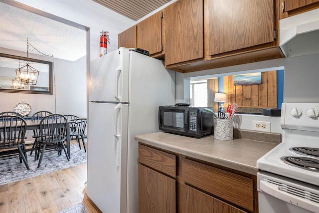 kitchen with light wood-style flooring, brown cabinetry, a notable chandelier, white appliances, and a textured ceiling