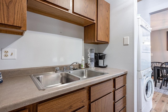 kitchen with brown cabinets, light wood-style floors, stacked washer and clothes dryer, and a sink