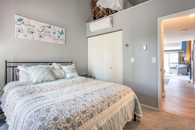 bedroom with a closet, light colored carpet, baseboards, and a wall unit AC