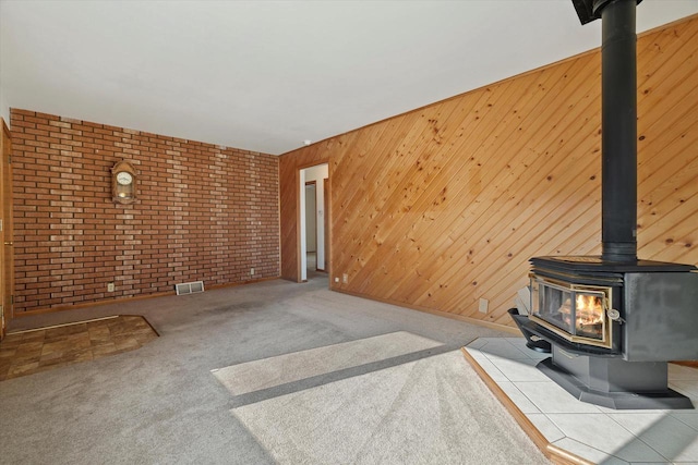 unfurnished living room with visible vents, carpet flooring, brick wall, and a wood stove