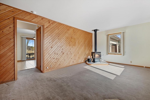 unfurnished living room with baseboards, carpet floors, wooden walls, and a wood stove