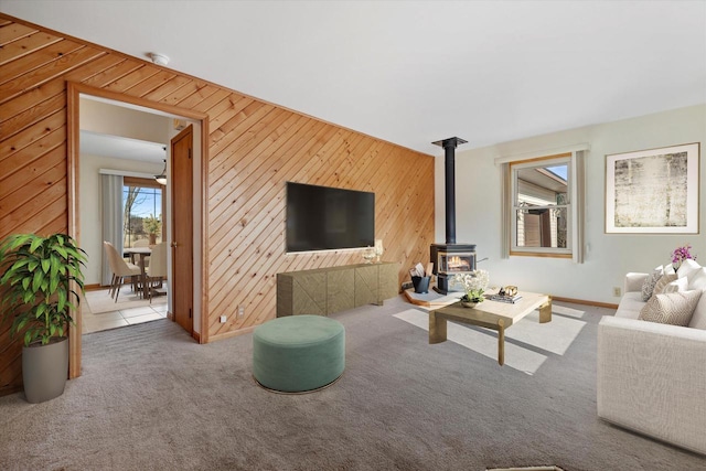 carpeted living area featuring wooden walls and a wood stove