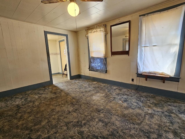 carpeted empty room featuring wooden walls and a ceiling fan