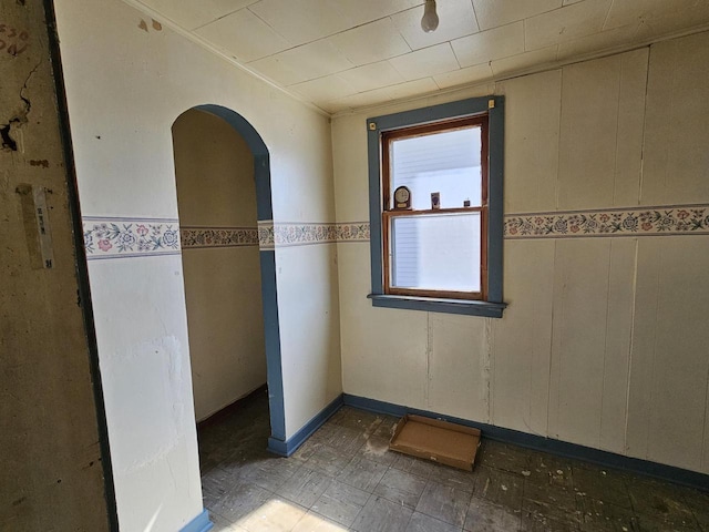 empty room with tile patterned floors, arched walkways, and wainscoting