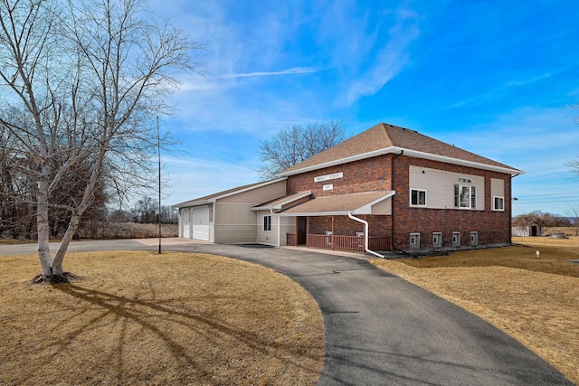 view of front facade featuring aphalt driveway, a front yard, a shingled roof, a garage, and brick siding