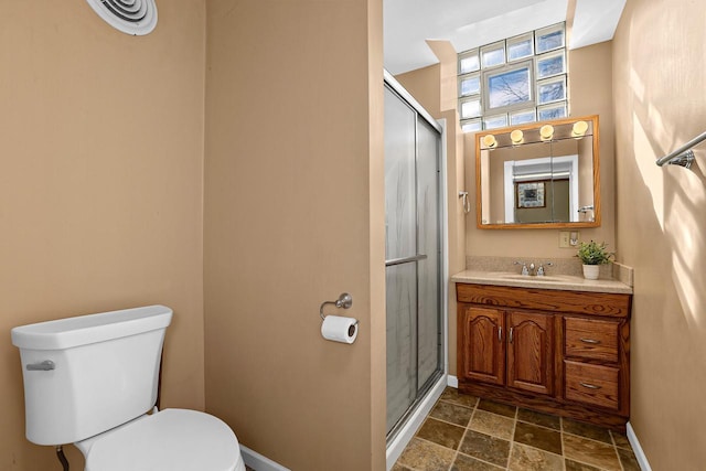 bathroom with a stall shower, toilet, vanity, and baseboards