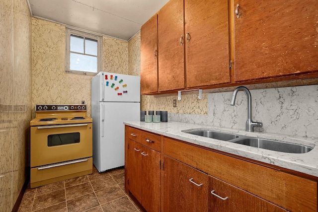 kitchen with a sink, tasteful backsplash, white appliances, brown cabinetry, and light stone countertops