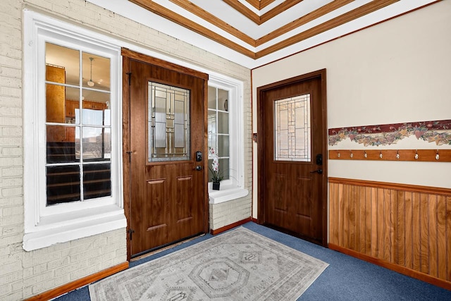 carpeted entryway featuring a wainscoted wall, wooden walls, brick wall, and ornamental molding