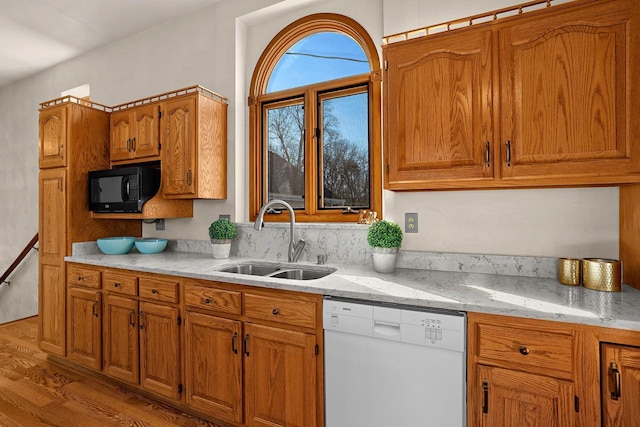 kitchen with brown cabinetry, light wood-style flooring, white dishwasher, a sink, and black microwave