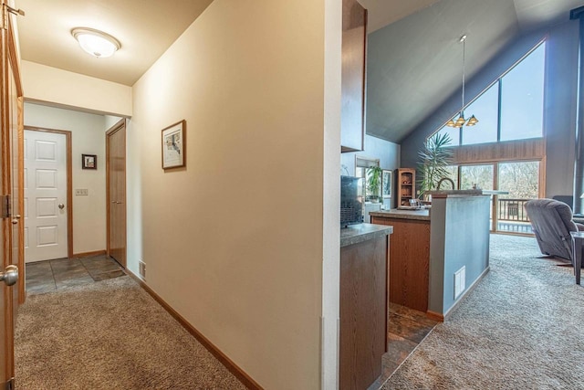 hall with visible vents, baseboards, high vaulted ceiling, and dark carpet