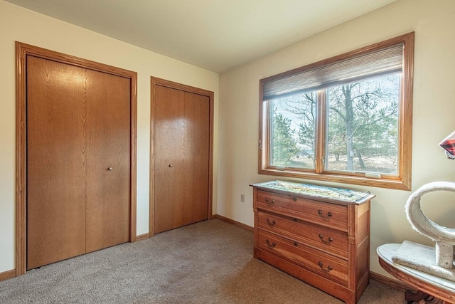 bedroom with light carpet, two closets, and baseboards