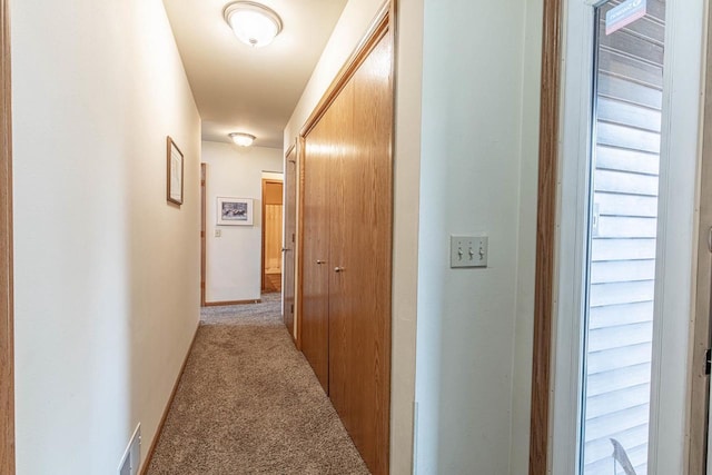 hallway with baseboards, visible vents, and light carpet