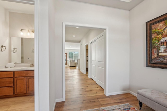 hallway with a sink, baseboards, and light wood finished floors