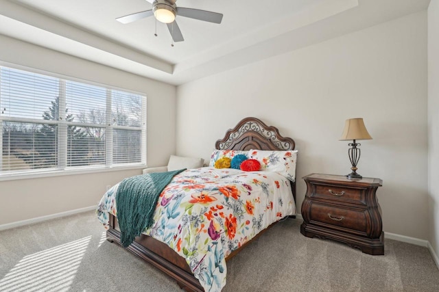 carpeted bedroom with a raised ceiling, a ceiling fan, and baseboards