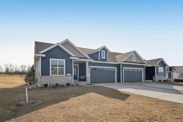 craftsman-style house featuring a front yard, roof with shingles, a garage, stone siding, and driveway