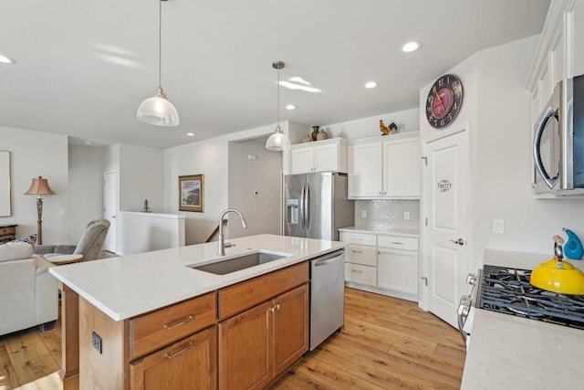 kitchen with light wood finished floors, a sink, open floor plan, stainless steel appliances, and light countertops