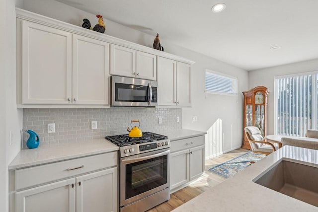 kitchen with backsplash, light wood-type flooring, recessed lighting, stainless steel appliances, and white cabinetry