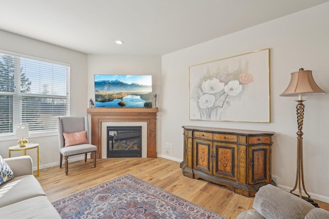 living room with recessed lighting, a glass covered fireplace, light wood-style flooring, and baseboards