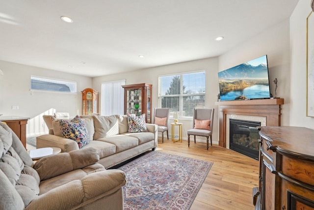 living room with a glass covered fireplace, recessed lighting, light wood-type flooring, and baseboards