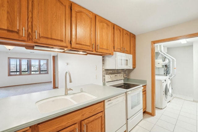 kitchen with white appliances, brown cabinetry, a sink, light countertops, and washer and dryer