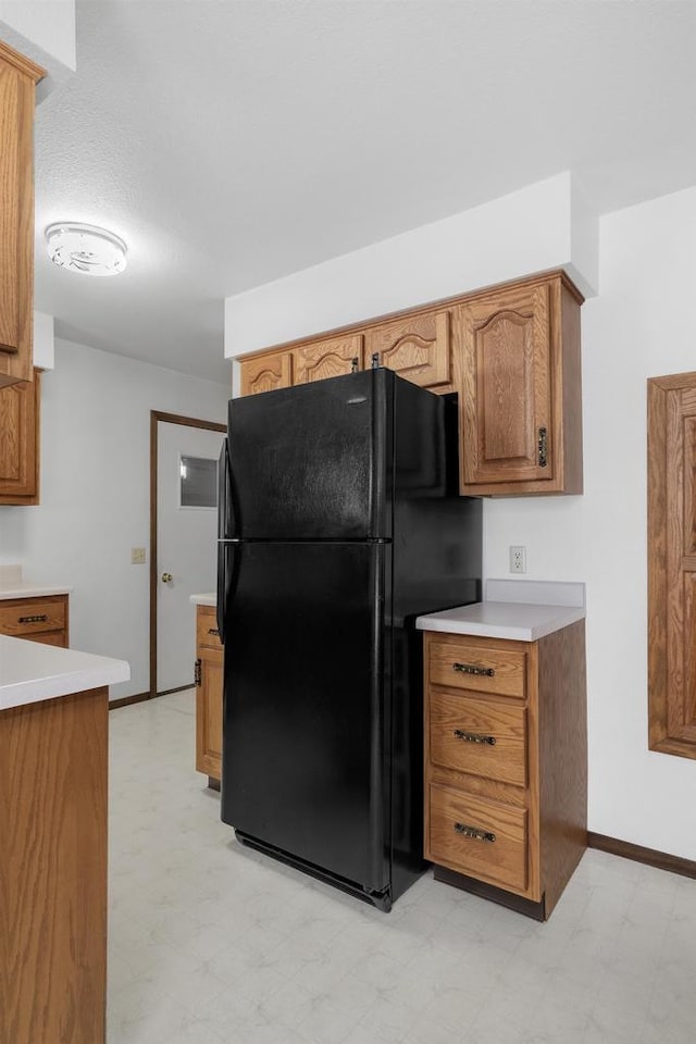 kitchen with light countertops, light floors, brown cabinets, and freestanding refrigerator